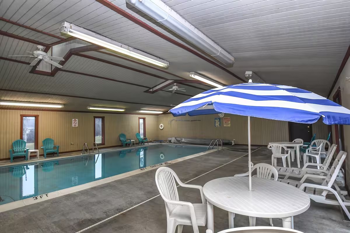 Indoor swimming pool at the second stay with tables, chairs, and a striped patio umbrella.