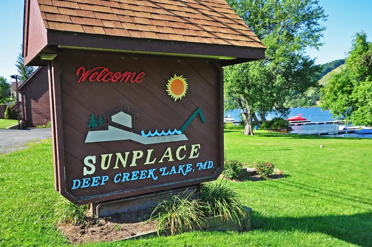 Sunplace Deep Creek Lake welcome sign with green lawn and docks visible behind it.